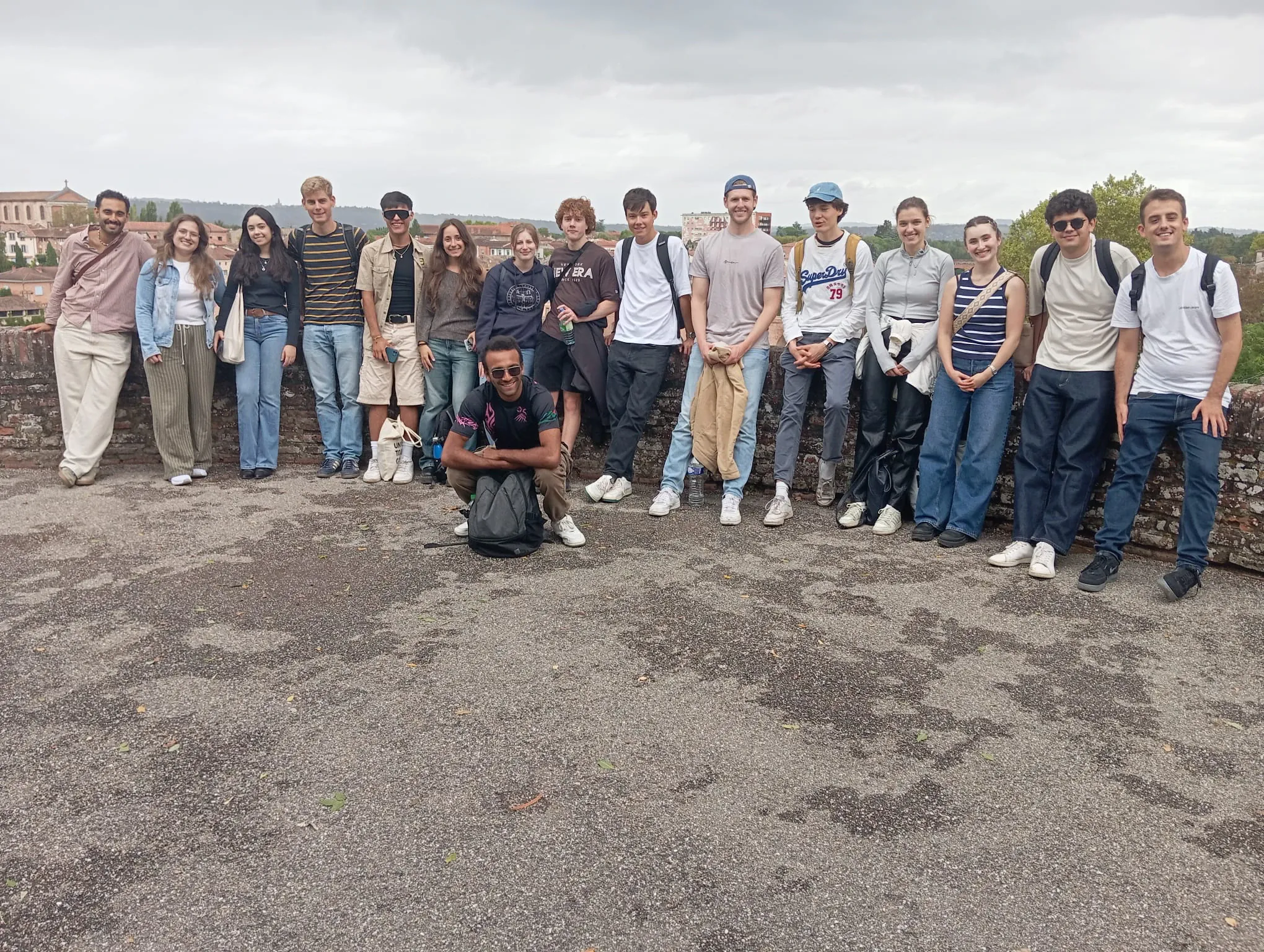 A large group standing along stone ramparts overlooking a town's rooftops