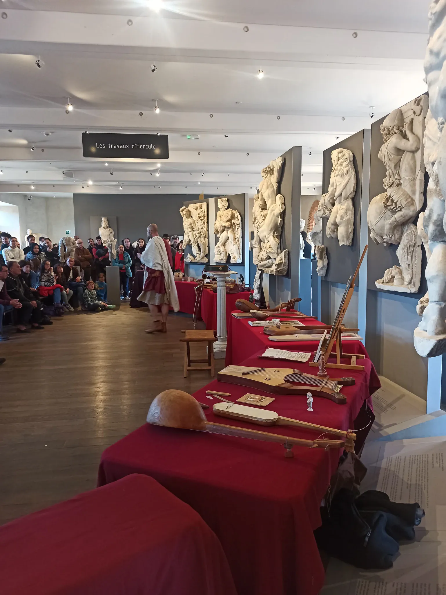 A guide talking to a seated group in a museum room lined with antique sculptures