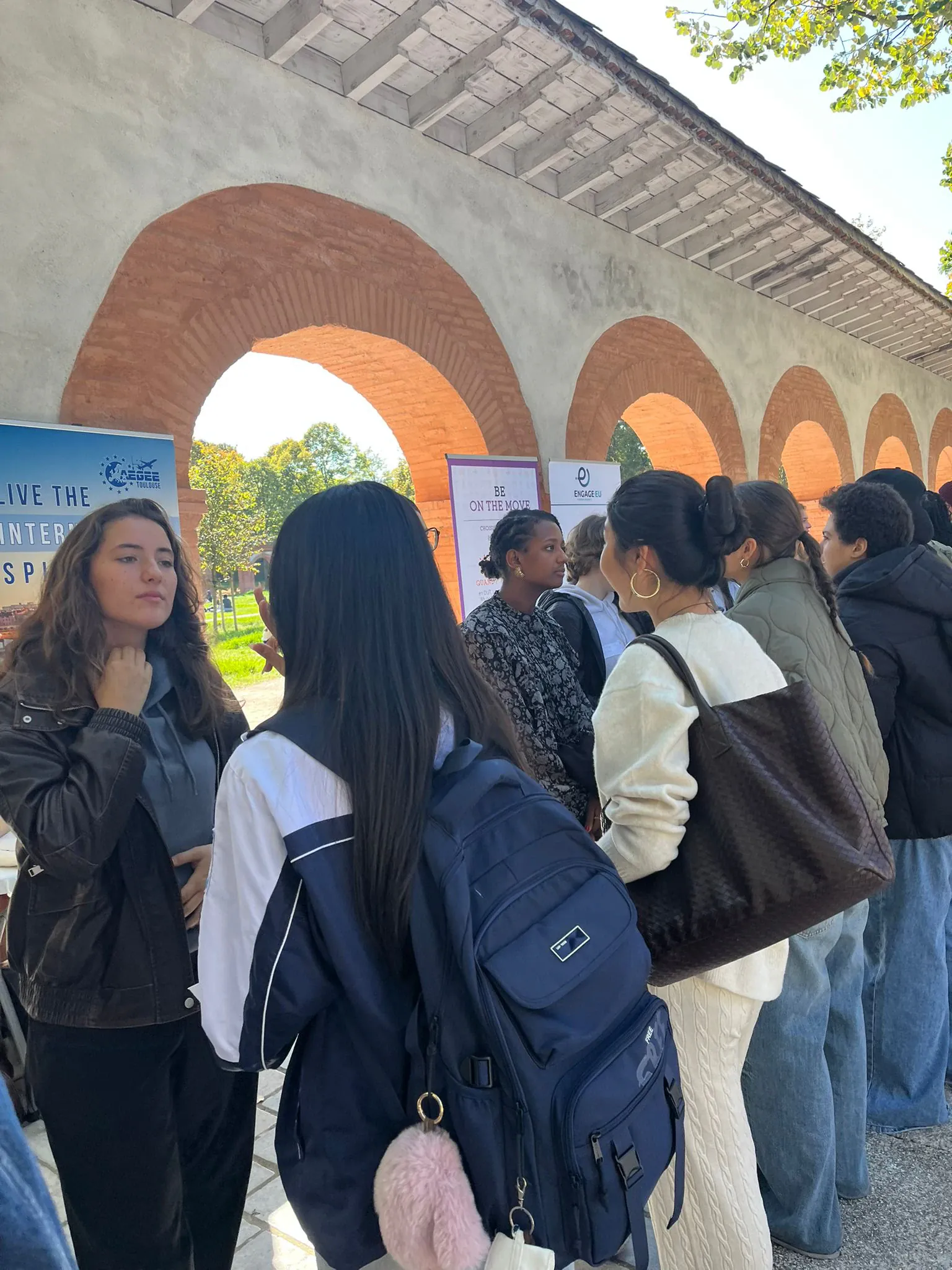 Students queueing past a row of association information stands under a covered walkway