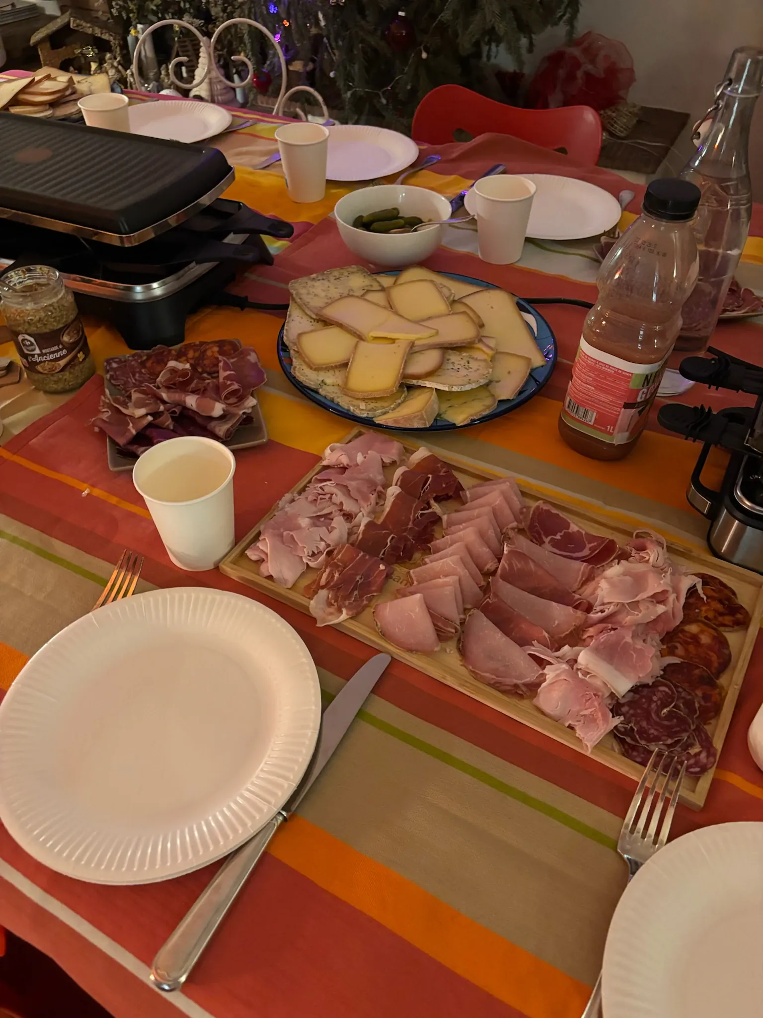 A table set for raclette, with a raclette machine, a cheese platter and cured meats