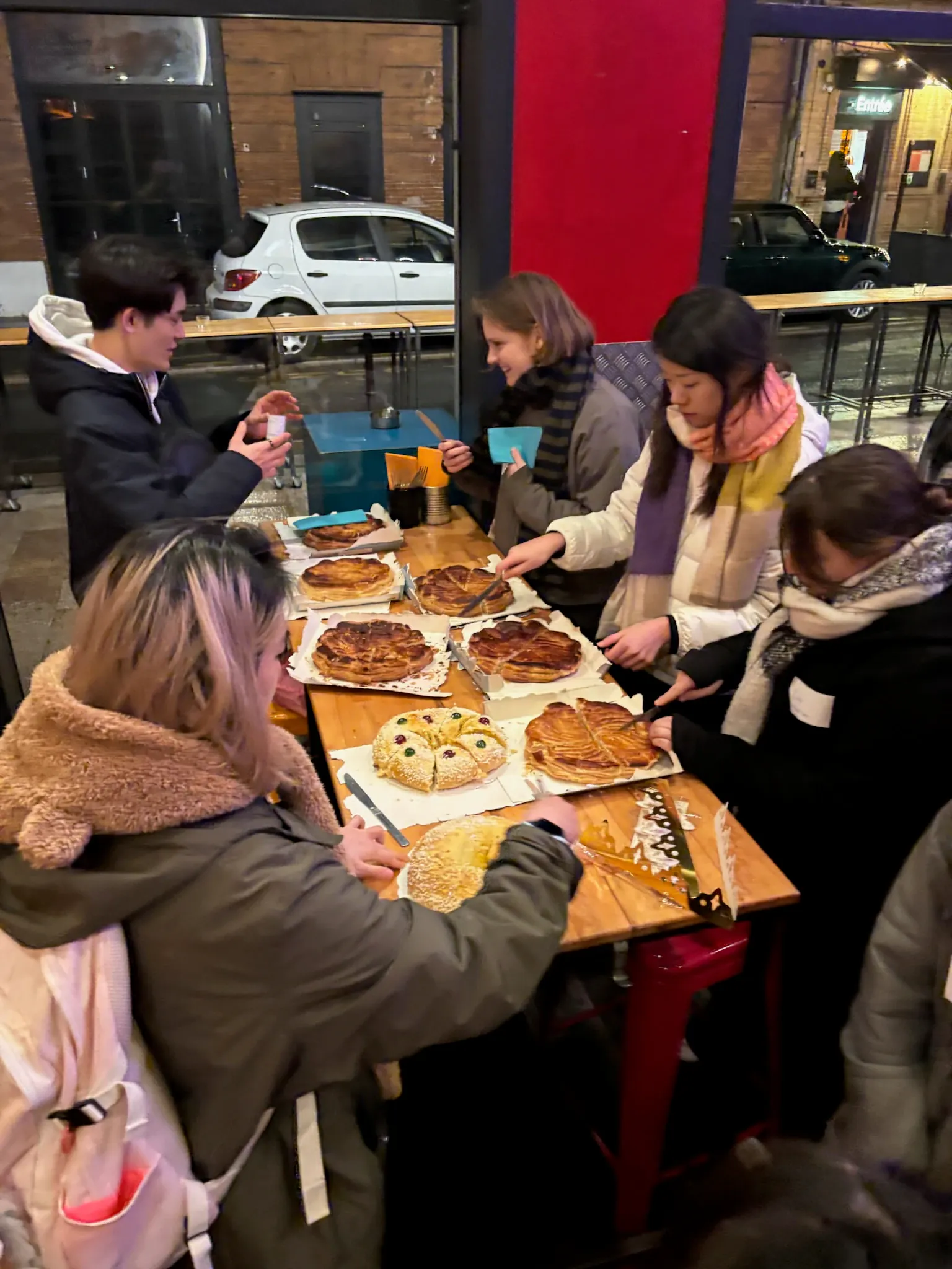 A group gathered around a table cutting into several galette des rois cakes