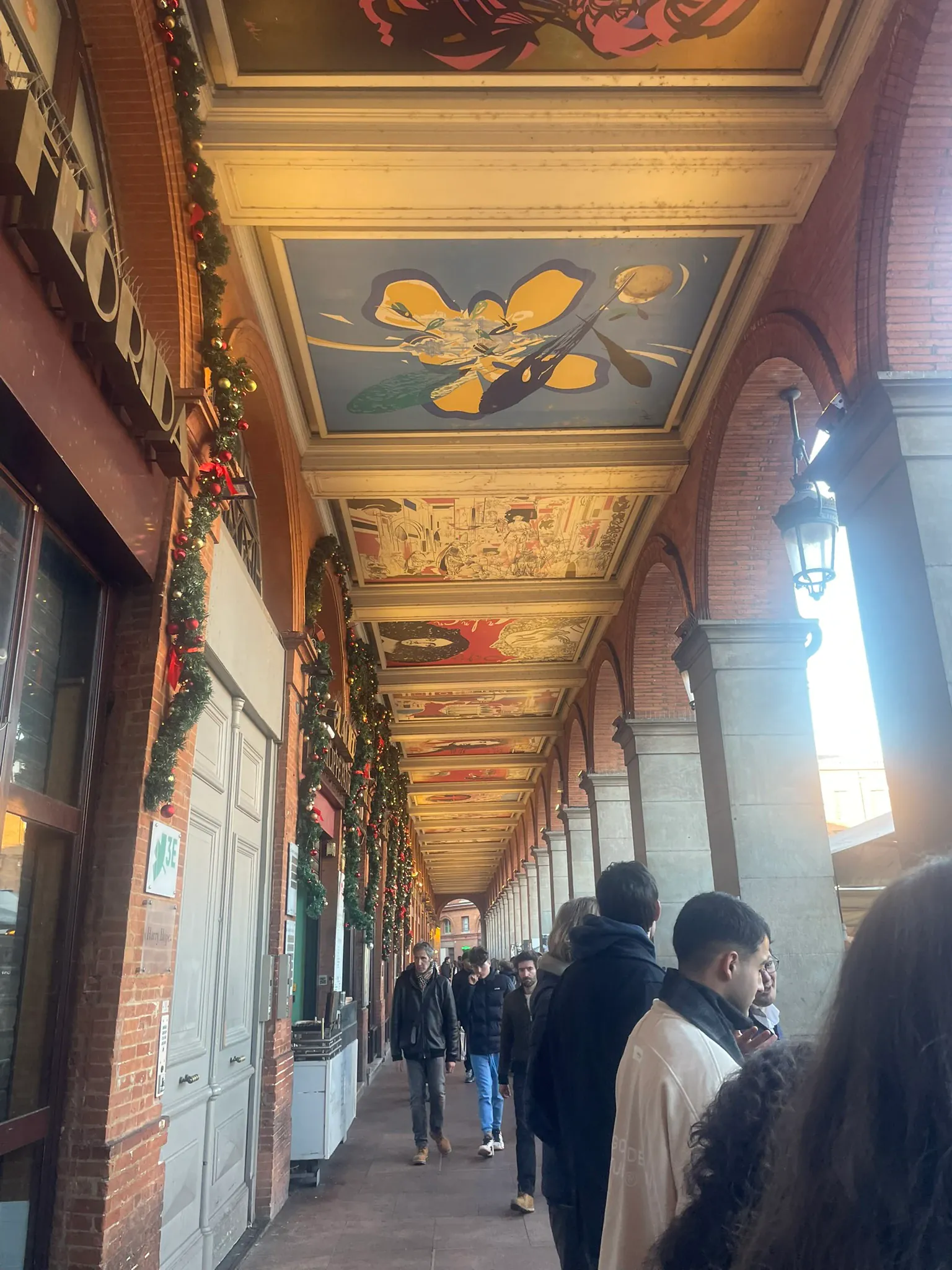 A group walking through a covered gallery with a painted ceiling