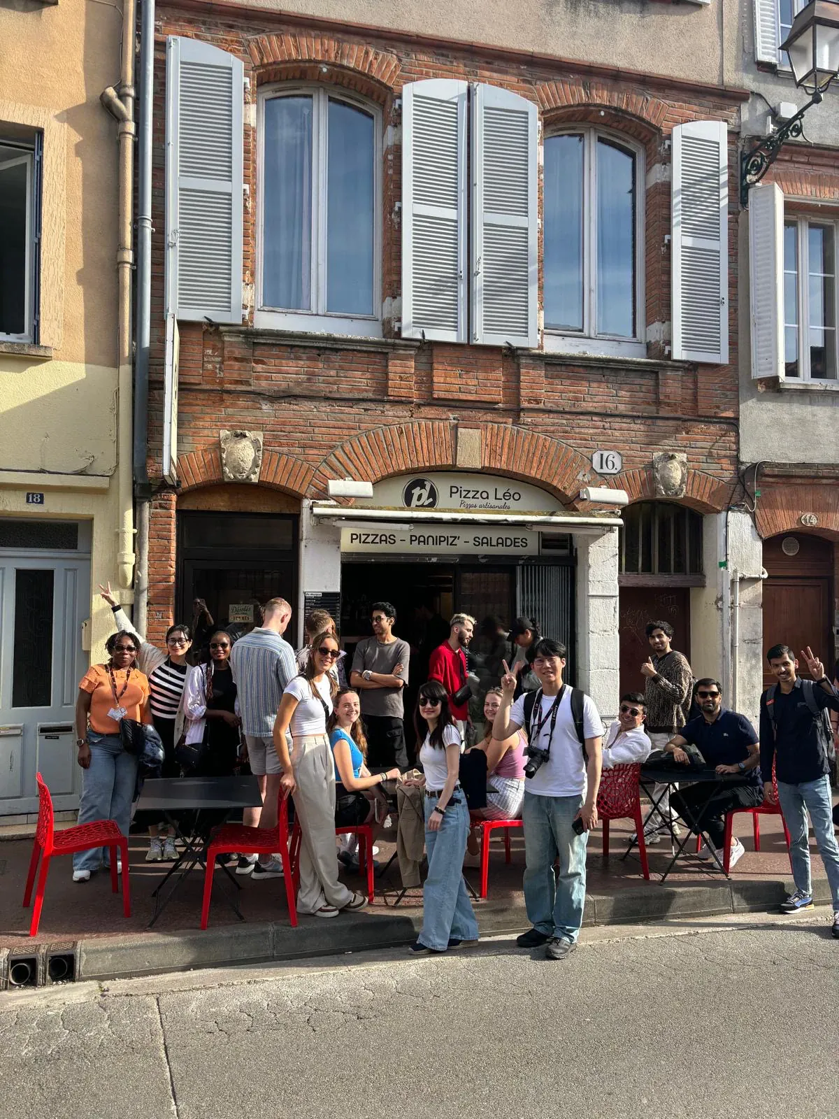 A group seated at an outdoor pizzeria terrace with red chairs, at the end of a walking tour