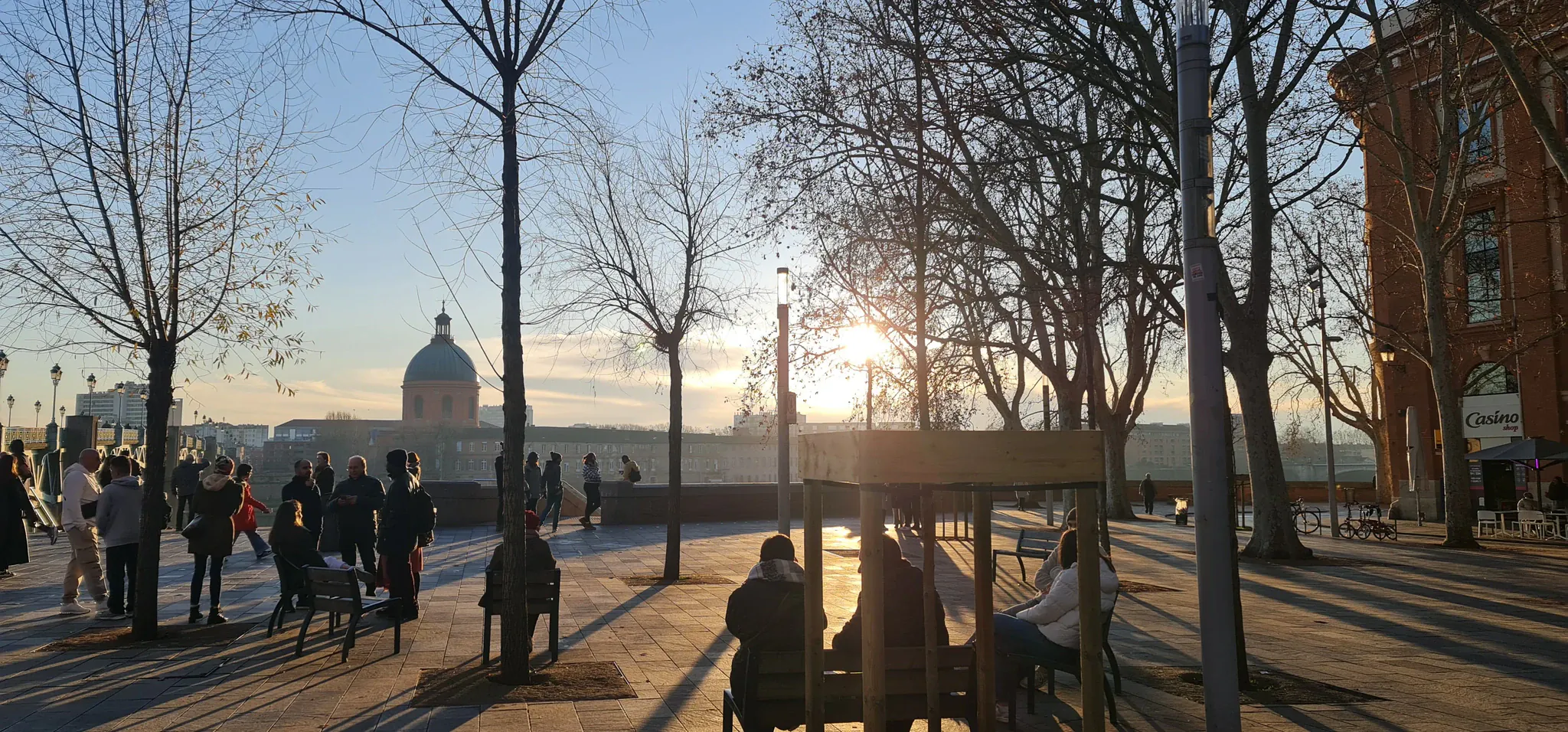 The Garonne quays at sunset, passers-by along the water and the dome of La Grave hospital in the distance