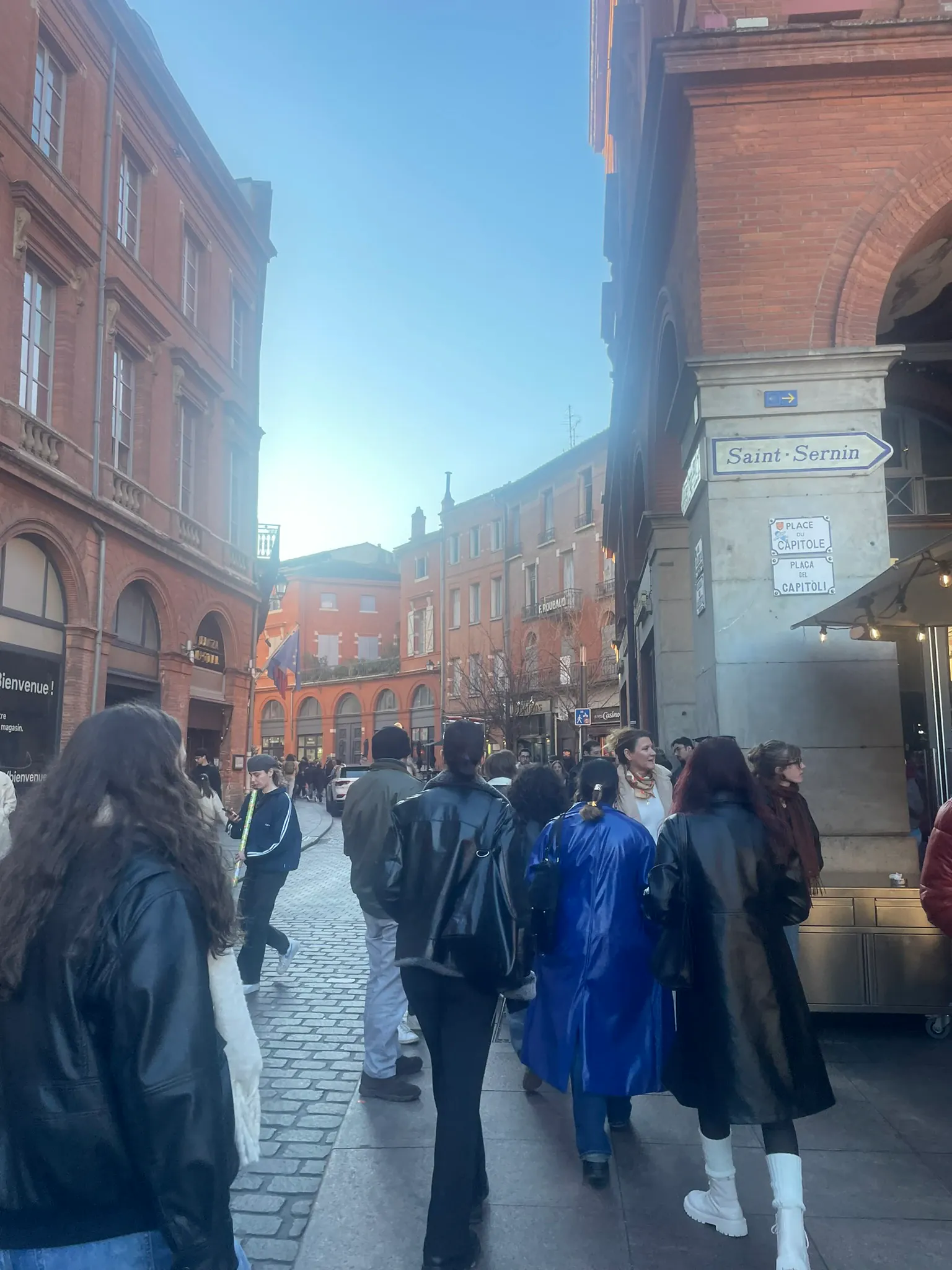 A group seen from behind, walking down a brick-paved street with a street sign in the foreground